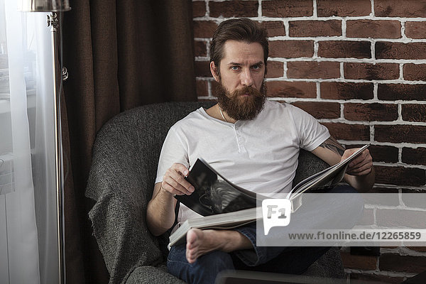 Portrait of man sitting on armchair with coffee-table book