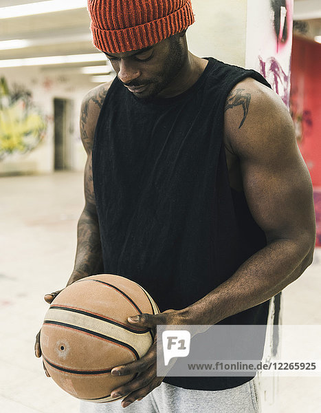 Mann mit Tattoos und Wollmütze hält Basketball