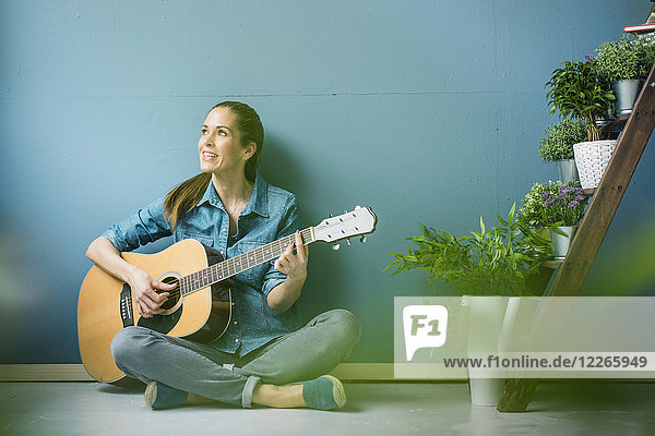 Frau entspannt in ihrem Haus mit Topfpflanzen,  Gitarre spielen