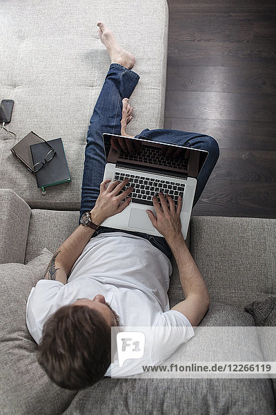 Mann auf der Couch zu Hause mit Laptop,  Draufsicht