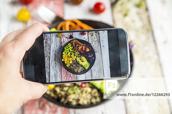 Mädchen fotografiert vegane Mittagsschale mit Handy  Nahaufnahme