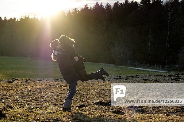 Glückliches junges Paar  das sich auf dem Feld gegen die Sonne küsst.
