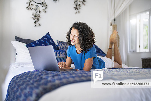 Lächelnde Frau im Bett liegend mit Laptop