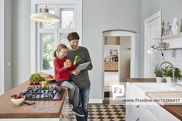 Smiling father and daughter with bell pepper and tablet in kitchen