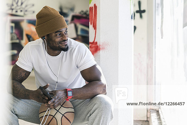 Lächelnder Mann mit Basketball  Smartphone und Kopfhörer