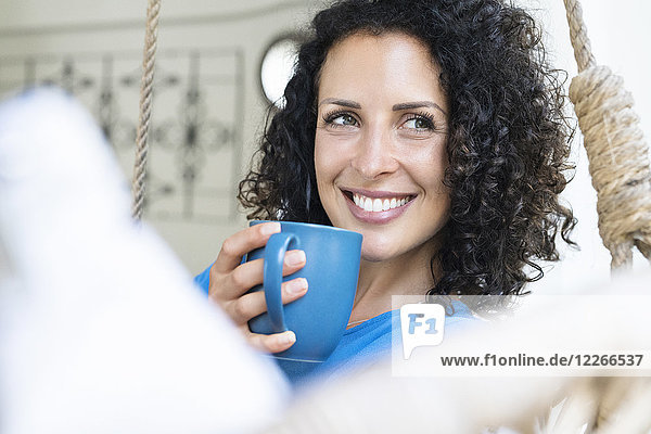 Lächelnde Frau mit lockigem Haar  die eine Tasse Kaffee hält.