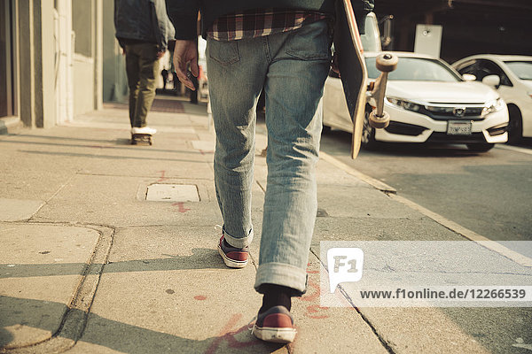 Low section of man walking on sidewalk with skateboard
