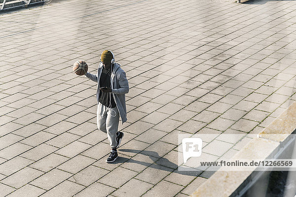 Young man with basketball walking on a square