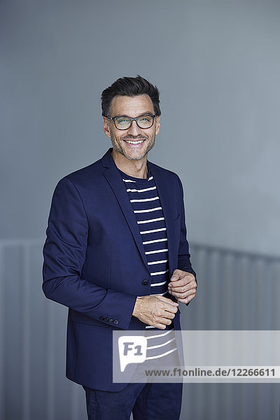 Porträt eines lächelnden Geschäftsmannes mit Stoppel im blauen Anzug und Brille