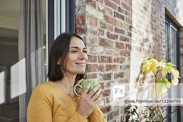 Lächelnde Frau trinkt aus Tasse vor ihrem Haus