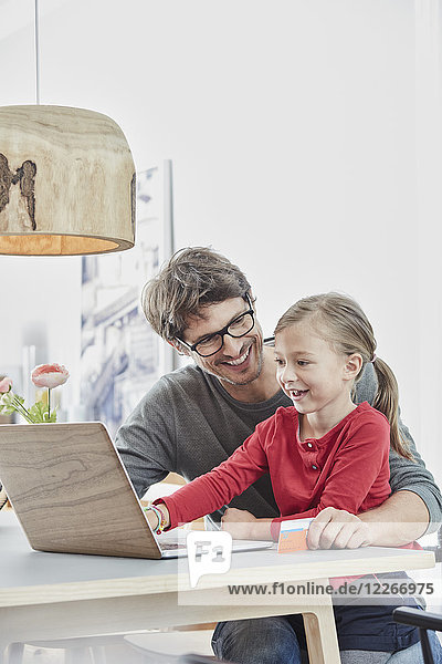 Glückliche Vater und Tochter mit einer Karte mit Laptop auf dem Tisch zu Hause