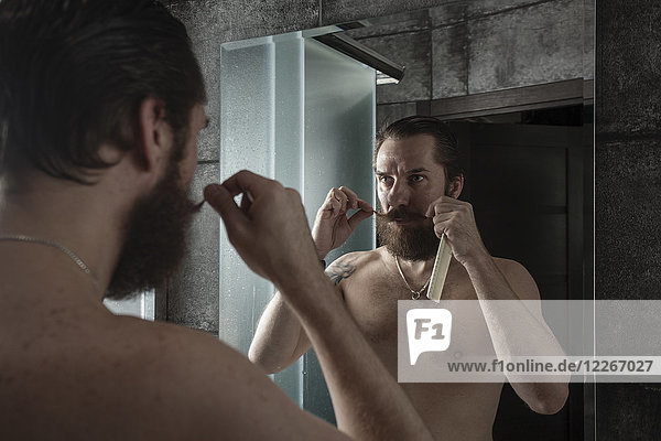 Portrait of bearded man looking at his mirror image while twirling his beard