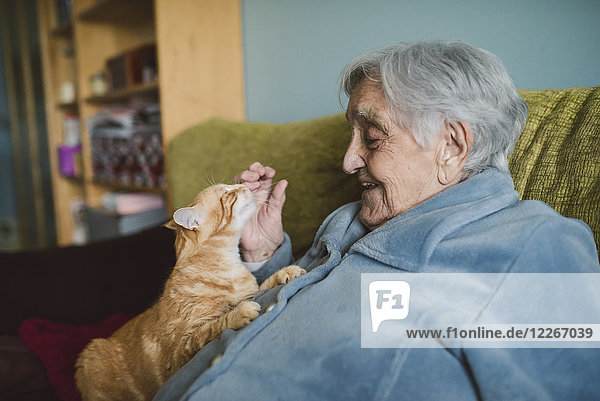 Fröhliche Seniorin mit Tabbykatze auf der Couch