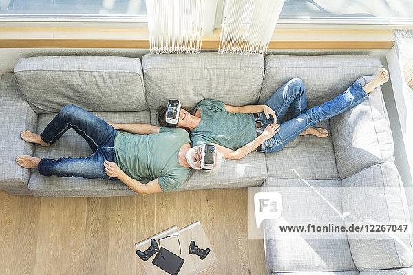 Glückliches reifes Paar das zu Hause auf der Couch liegt und eine VR-Brille trägt.