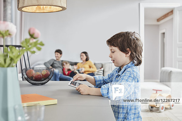 Boy looking at tablet at home with family in background