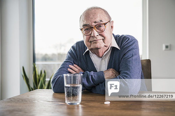 Portrait of senior man sitting at table with pill and glass of water