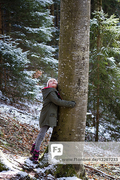 Mädchen umarmen Baum im Wald im Winter
