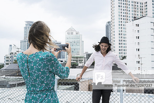 Junge Frau mit Smartphone beim Fotografieren des Freundes auf dem Dach