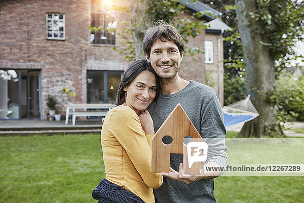 Portrait of smiling couple in garden of their home holding house model