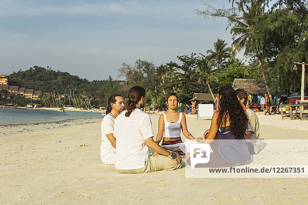 Thailand  Koh Phangan  Gruppe von Menschen  die gemeinsam an einem Strand meditieren.