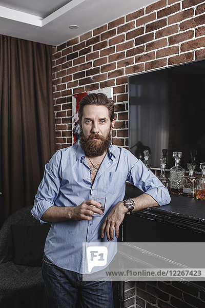 Portrait of bearded man with glass of whiskey at home