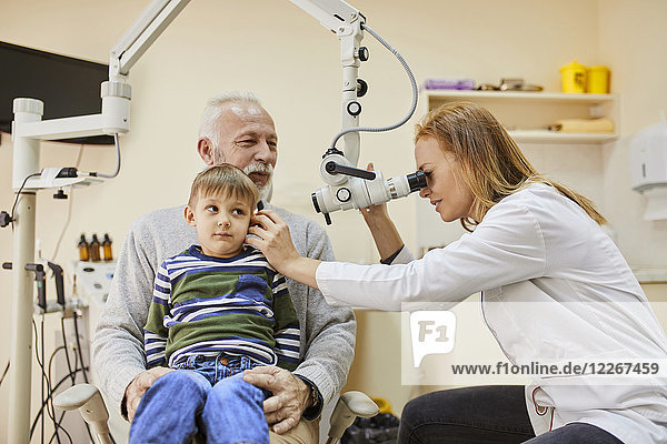 HNO-Arzt untersucht Ohr eines Jungen auf Großvaters Schoß