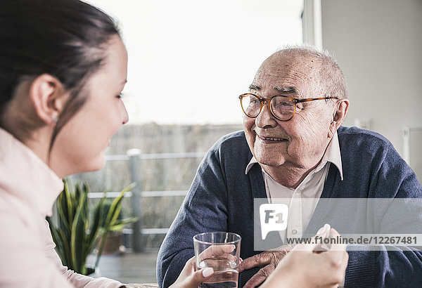 Frau hält Pille und Glas Wasser für lächelnden älteren Mann