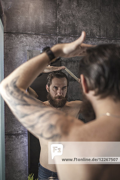 Portrait of bearded man looking at his mirror image while combing his hair
