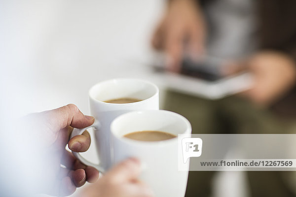 Close-up of woman holding coffee cups while man using tablet in office