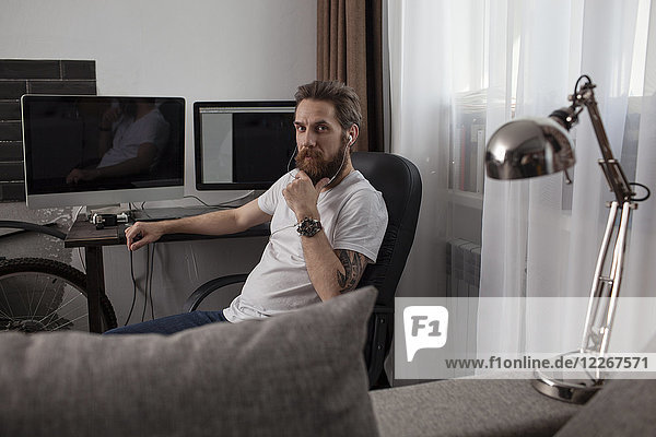 Portrait of bearded man sitting in the living room listening music with earphones