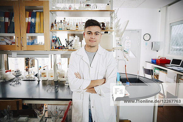 Porträt eines selbstbewussten jungen,  männlichen Studenten mit gekreuzten Armen im Chemielabor