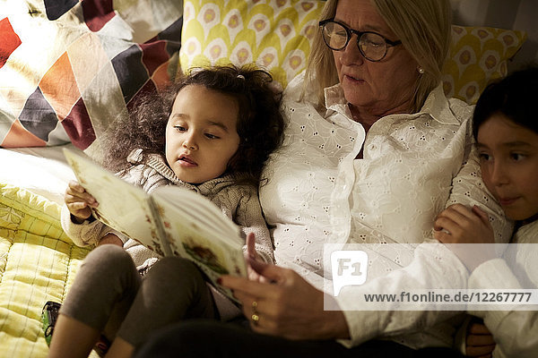 Hochwinkelansicht von Großmutter Lesebuch zu Enkelinnen im Liegen zu Hause