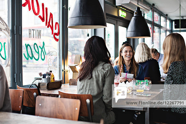 Smiling female friends enjoying while sitting at dining table for brunch in restaurant