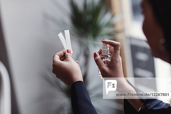 Cropped image of woman spraying perfume on litmus strips at workshop