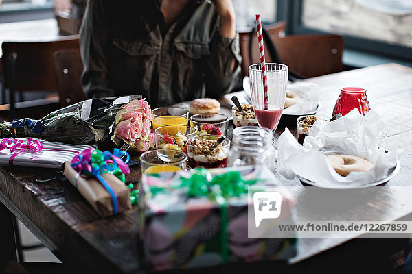 Midsection of young woman sitting with birthday presents and food on restaurant