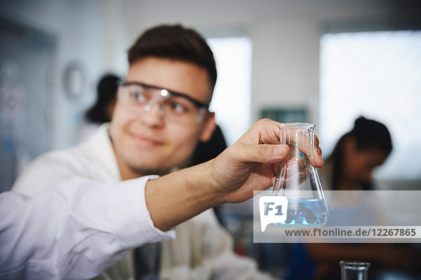 Abgeschnittene Hand des männlichen Studenten  der die Lösung in einem konischen Kolben hält  von einem Freund im Chemielabor.