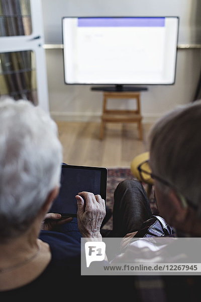 Rückansicht des Seniorenpaares mit digitalem Tablett  das zu Hause fernsieht.