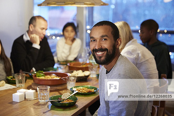 Porträt eines lächelnden Vaters  der mit seiner Familie beim Essen am Tisch sitzt.