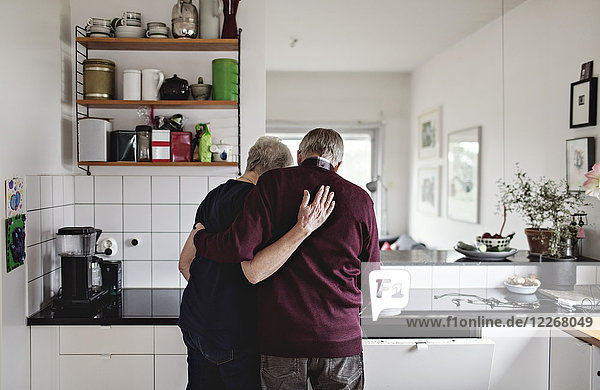 Rückansicht des pensionierten Seniorenpaares  das in der Küche zu Hause steht.