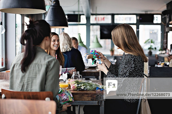 Lächelnde weibliche Freunde  die die Frau beim Sitzen am Esstisch im Restaurant ansehen.