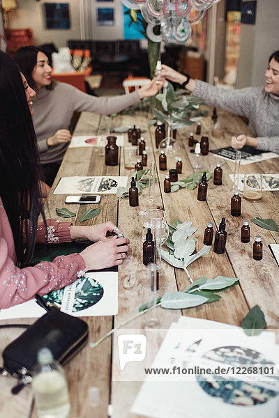 Lächelnde Kolleginnen am Tisch mit Parfümflaschen in der Werkstatt