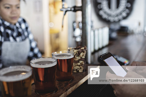 Kundin beim kontaktlosen Bezahlen per Smartphone an die Barkeeperin für Bier am Schalter