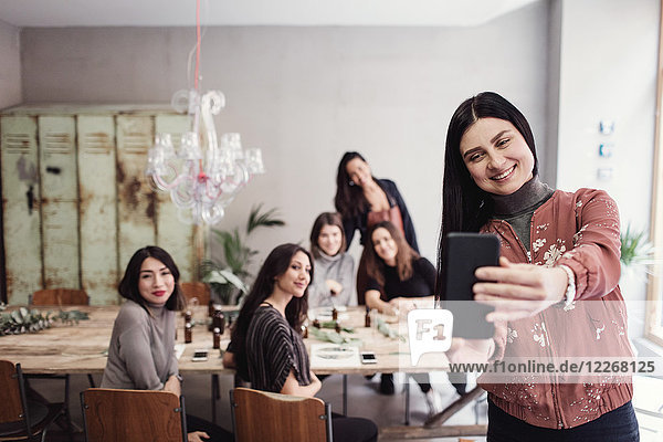 Lächelnde Frau nimmt Selfie mit weiblichen Kollegen in der Werkstatt mit