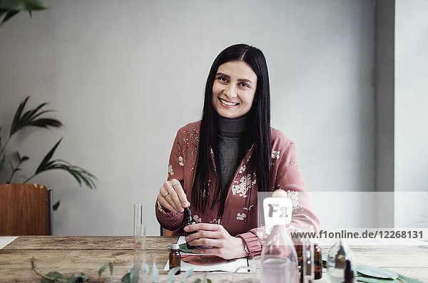 Porträt einer lächelnden Unternehmerin bei der Zubereitung von Parfüm am Tisch in der Werkstatt