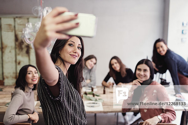 Lächelnde junge Frau nimmt Selfie mit weiblichen Mitarbeitern in der Werkstatt mit.