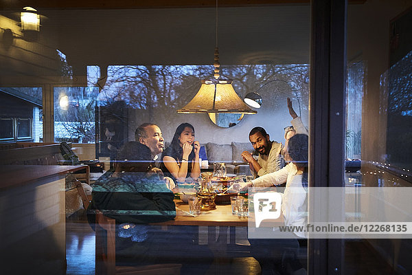 Mehrgenerationen-Familiengespräch beim Abendessen am Tisch durchs Fenster gesehen