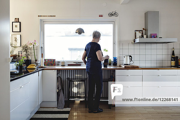 Full length rear view of senior woman standing in kitchen at home