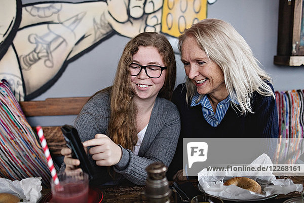 Lächelnde Tochter zeigt der Frau ein Smartphone  während sie am Esstisch sitzt.