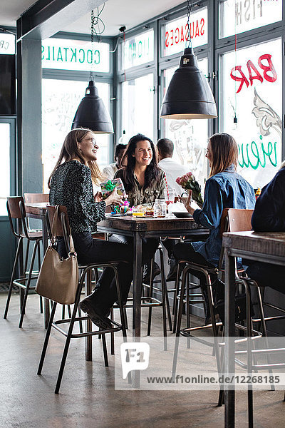 Full length of smiling female friends sitting with birthday presents at dining table in restaurant