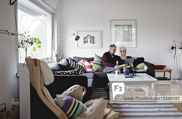 Seniorenpaar sitzt auf dem Sofa und teilt sich ein digitales Tablett im Wohnzimmer zu Hause.